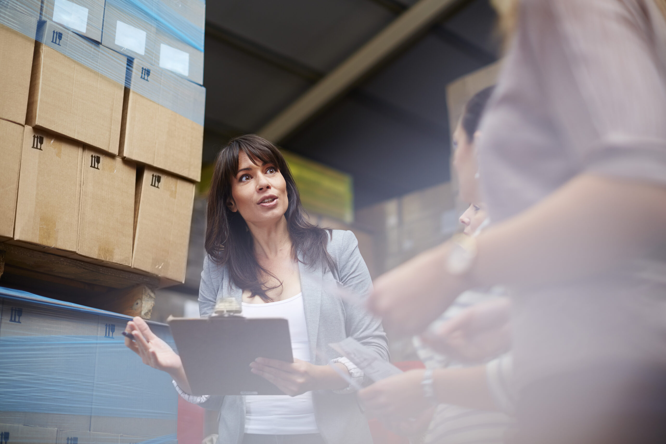 Woman with clipboard in warehouse talking to women